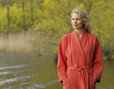 Blonde Frau trägt Bio Waffelpikee-Bademantel in Korallen-Rot am See und steht auf einem Steg